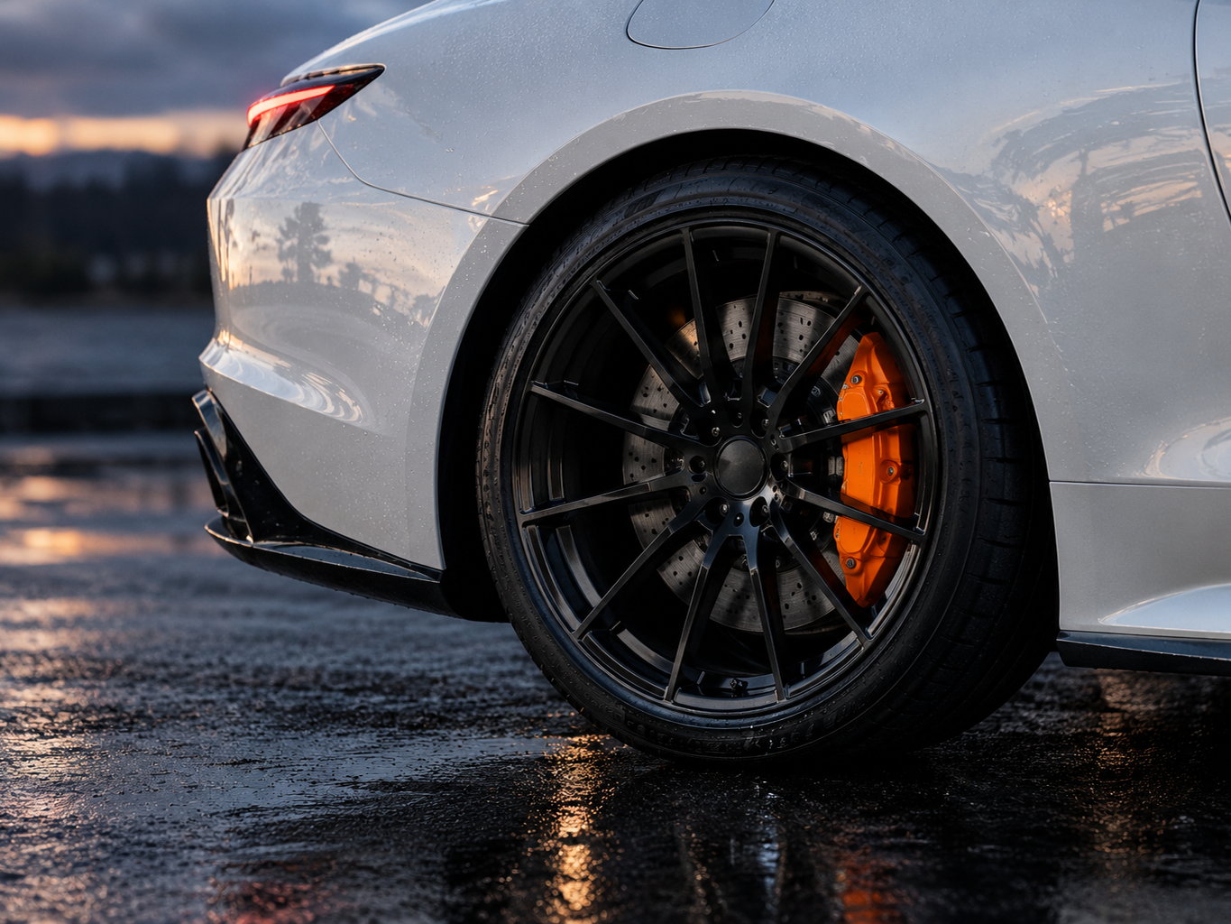 A white car's rear wheel and orange caliper, close